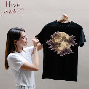May include: A black short-sleeved t-shirt featuring a graphic print of a full moon surrounded by dark purple clouds. The text Hive print is visible in the upper left corner of the image. The garment has a crew neckline and a standard fit.