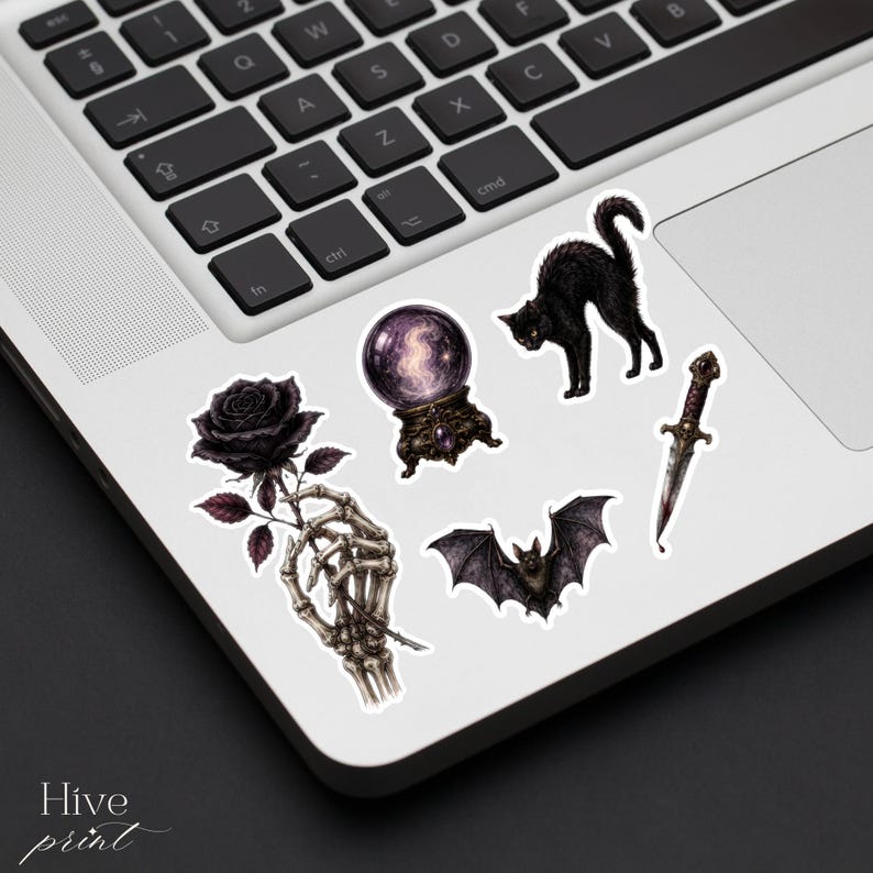 May include: A collection of five individual stickers featuring a skeletal hand holding a black rose, a glowing purple crystal ball, a black cat with an arched back, a flying bat, and a silver dagger with a dark handle, all arranged on a laptop.