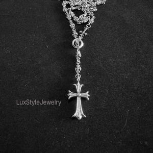 May include: A silver-toned necklace with a cross pendant. The necklace features a detailed chain design with small cross accents and a larger cross pendant at the bottom. The text "LuxStyleJewelry" is visible in the lower left corner.