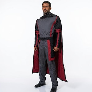 Pode incluir: Um traje cinza e vermelho com uma capa preta. O traje inclui uma parte superior de manga comprida, cal&ccedil;as e uma capa com forro vermelho. A pessoa est&aacute; usando sapatos pretos.