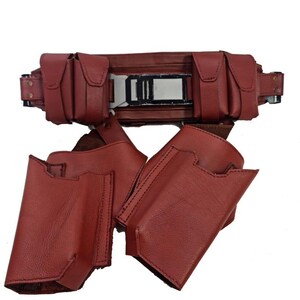 May include: A burgundy leather utility belt with multiple pouches and a rectangular buckle. The belt features several small, square pouches and two larger holster-like pouches. The leather appears to be stitched with a darker thread.