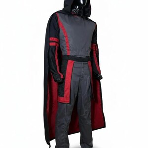 Pode incluir: Uma fantasia com capa com capuz e roupa a condizer. A capa &eacute; preta com interior vermelho, e a roupa &eacute; principalmente cinzenta com detalhes vermelhos. A fantasia &eacute; exibida num manequim sobre um fundo branco.