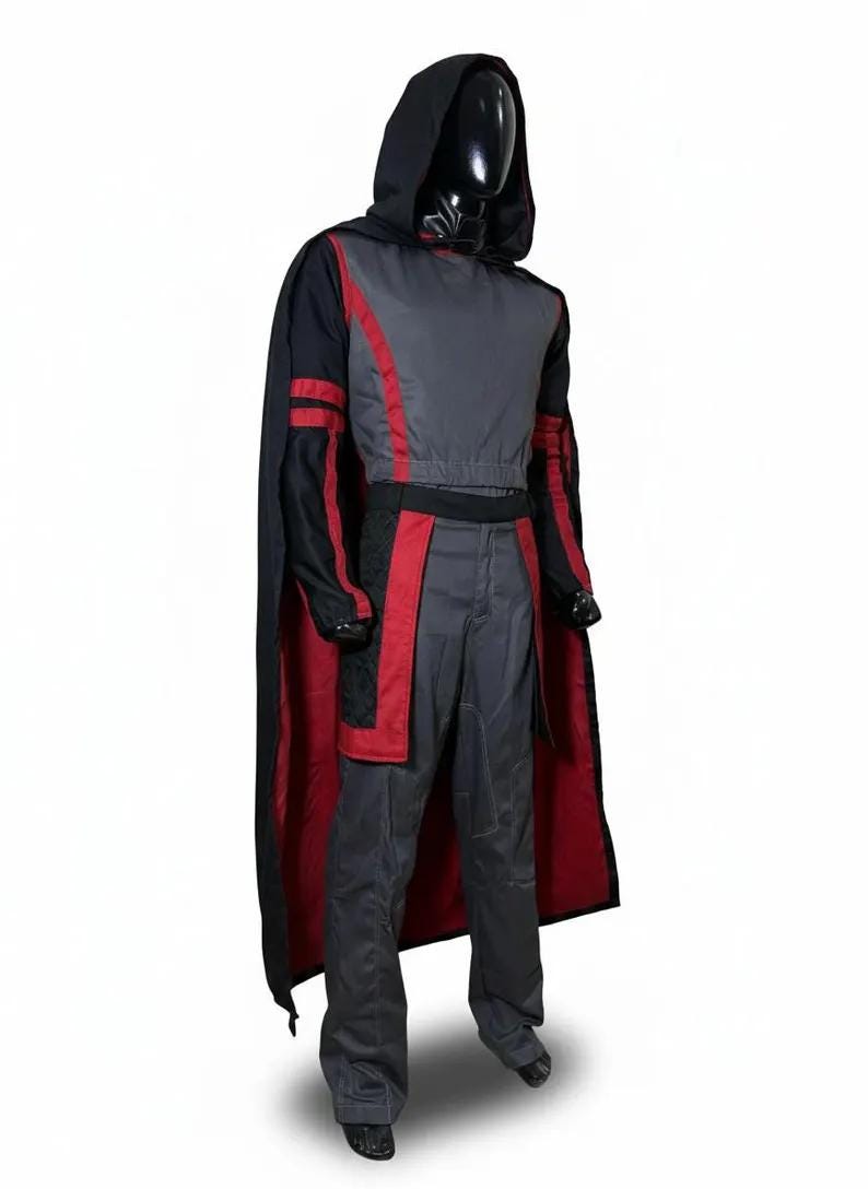 Pode incluir: Uma fantasia com capa com capuz e roupa a condizer. A capa &eacute; preta com interior vermelho, e a roupa &eacute; principalmente cinzenta com detalhes vermelhos. A fantasia &eacute; exibida num manequim sobre um fundo branco.