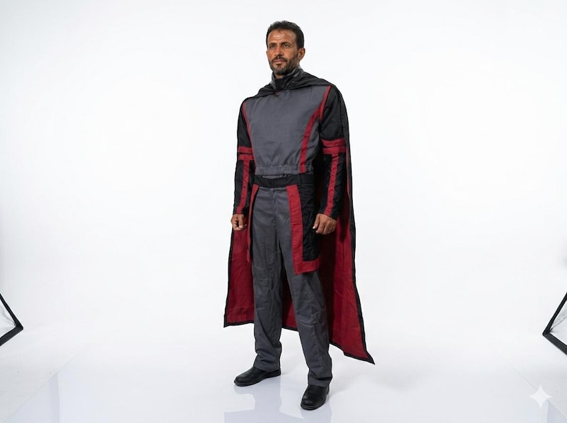 Pode incluir: Um traje cinza e vermelho com uma capa preta. O traje inclui uma parte superior de manga comprida, cal&ccedil;as e uma capa com forro vermelho. A pessoa est&aacute; usando sapatos pretos.