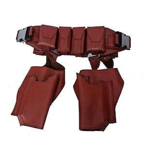 May include: A brown leather utility belt with multiple pouches and pockets. The belt features a silver buckle and two additional pouches hanging below. The design is symmetrical and appears to be made of high-quality leather.
