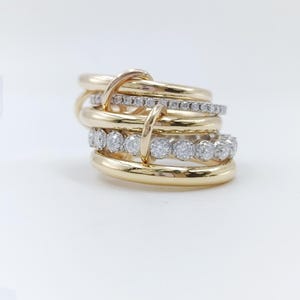 Puede incluir: Un conjunto de anillos de oro con detalles de diamantes. Los anillos están entrelazados, con bandas de oro liso y bandas engastadas con pequeños diamantes. El diseño es moderno y elegante, sobre un fondo blanco.