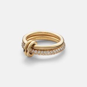 May include: Three gold rings. One ring is a band with a knot design, and the other is a band with small, clear stones. The third ring is a plain gold band. The rings are stacked together.