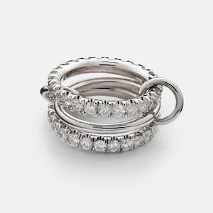 May include: A stackable silver ring set featuring multiple bands, each encrusted with small, sparkling gemstones. The rings are connected by a small silver loop, creating a unique and elegant design. The gemstones are clear and reflect light.