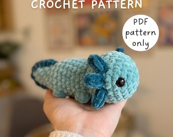 May include: A light blue crocheted axolotl plush toy with dark blue gills and black eyes. The text NO-SEW AXOLOTL CROCHET PATTERN and PDF pattern only is visible in the image. The plush has a soft, textured yarn appearance and a rounded body.