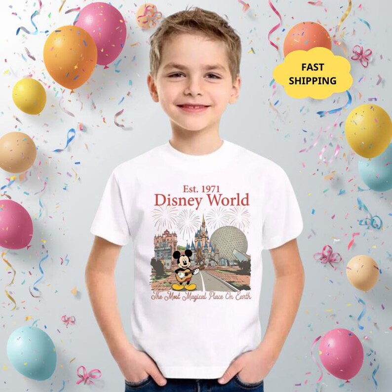 May include: A white t-shirt featuring a graphic of Mickey Mouse playing a guitar in front of Disney World landmarks. The shirt has the text "Est. 1971 Disney World" and "The Most Magical Place On Earth".