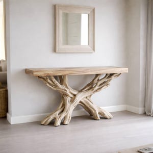 May include: A light-colored wooden console table with a natural, tree-branch-like base. The rectangular tabletop is supported by an intricate network of intertwined branches. A matching framed mirror hangs above the table on a white wall.