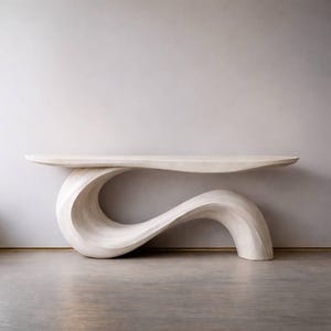 Może przedstawiać: Jasny, rzeźbiarski stolik konsolowy o unikalnym, płynnym designie. Stół posiada długi, płaski blat wsparty na pojedynczej, ciągłej, zakrzywionej podstawie. Podstawa ma falisty kształt, dodając meblom nowoczesnego charakteru.