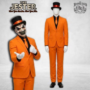 Può includere: Un abito arancione brillante composto da giacca, pantaloni e camicia nera con cravatta arancione. Il set include un cilindro nero con fascia arancione e guanti bianchi. Testo: THE JESTER Now You See Me. Now You Die. The Bespoke Guild BG.