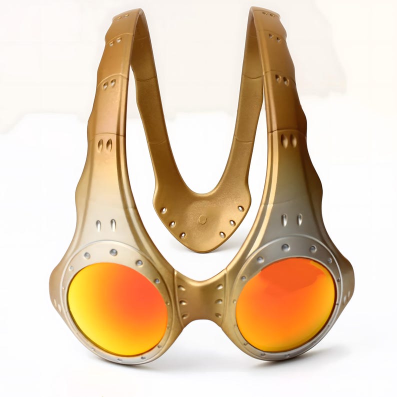 Authentische goldene Oakley Over-The-Top (OTT) Sonnenbrille auf weißem Grund. Das seltene Archive-Piece besticht durch einen matten Goldrahmen in skulpturalem Over-the-head Design. Die kreisrunden Spiegelgläser zeigen einen Verlauf von leuchtendem Gelbgold zu Orange. Mit industriellen Belüftungsschlitzen und Nieten-Details ist dieses Sammlerstück ein Highlight für Techwear-, Gorpcore- und Avantgarde-Enthusiasten sowie Oakley-Liebhaber.