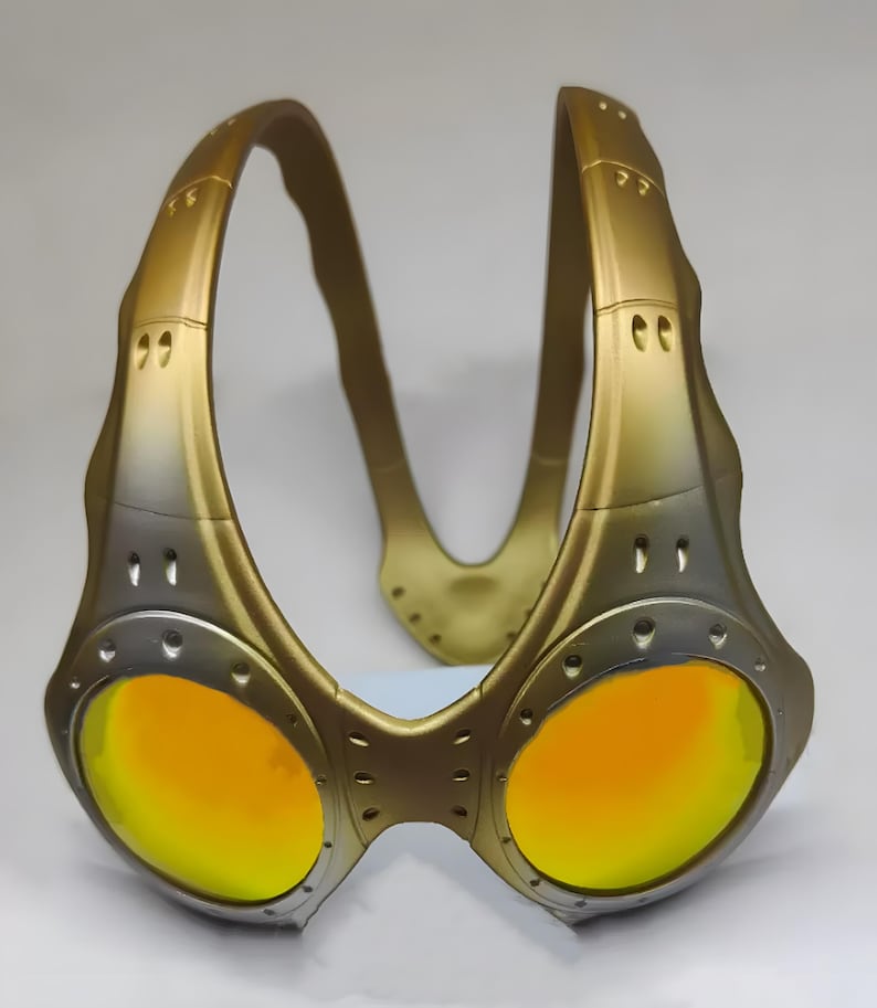 Authentische goldene Oakley Over-The-Top (OTT) Sonnenbrille auf weißem Grund. Das seltene Archive-Piece besticht durch einen matten Goldrahmen in skulpturalem Over-the-head Design. Die kreisrunden Spiegelgläser zeigen einen Verlauf von leuchtendem Gelbgold zu Orange. Mit industriellen Belüftungsschlitzen und Nieten-Details ist dieses Sammlerstück ein Highlight für Techwear-, Gorpcore- und Avantgarde-Enthusiasten sowie Oakley-Liebhaber.