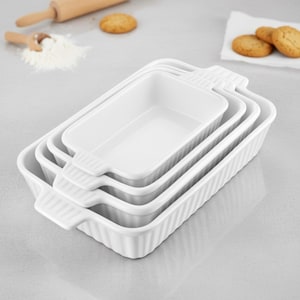 May include: A stack of four white rectangular baking dishes with ribbed sides and handles. The dishes are nested, with a rolling pin, flour, and cookies in the background. Ideal for baking.