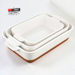 Könnte beinhalten: Ein Satz von drei weißen Keramik-Backformen, die ineinander verschachtelt sind. Die Formen haben eine gesprenkelte Innenseite, gerippte Seiten und braune Böden. Jede Form hat Griffe. Das Bild enthält auch den Text "FREE DELIVERY".