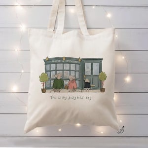Puede incluir: Bolso tote de color crema con una ilustración de ratones frente a una tienda verde con el texto "MOUSE & SPENCER". El texto "This is my picky bits' bag" está impreso debajo. Firma del artista en la esquina inferior derecha.