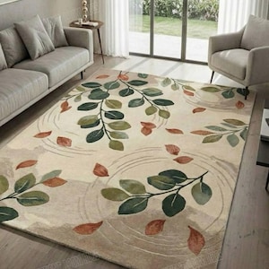 以下が含まれることがあります： ベージュ色のラグで、植物のデザインが施されています。ラグには、緑と茶色の葉と赤茶色の葉のアクセントがあります。デザインには同心円が含まれており、水のような効果を生み出しています。ラグは木製の床に置かれています。