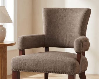May include: An armchair upholstered in a textured brown fabric featuring a curved backrest, padded armrests, and dark wooden legs. The base of the seat and the armrests are accented with a row of small, metallic nailhead trim details.