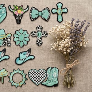 May include: A collection of embroidered patches in turquoise, black, and white, featuring designs of bandanas, cow skulls, bows, crosses, cowboy hats, flowers, saddles, and boots, alongside a dried bouquet of baby's breath and lavender flowers.