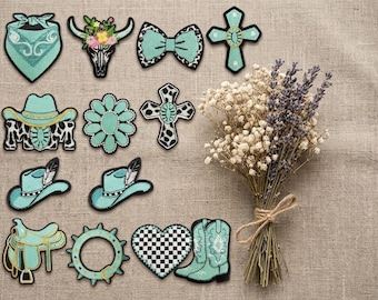 May include: A collection of embroidered patches in turquoise, black, and white, featuring designs of bandanas, cow skulls, bows, crosses, cowboy hats, flowers, saddles, and boots, alongside a dried bouquet of baby's breath and lavender flowers.