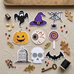 May include: A collection of embroidered Halloween patches including a black ghost, purple witch hat, spider web, orange pumpkin, eyeball, purple and yellow lollipop, grey tombstone with text trick or treat, white skull, and a black bat.
