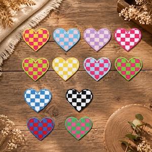 Puede incluir: Una colección de once parches bordados en forma de corazón, cada uno con un patrón de cuadros bicolor distinto. Los colores incluyen amarillo y rosa, azul claro y blanco, lavanda y blanco, rosa fuerte y blanco, verde lima y rosa, amarillo y blanco, azul y rosa, verde y rosa, azul y blanco, negro y blanco, y rojo y azul.