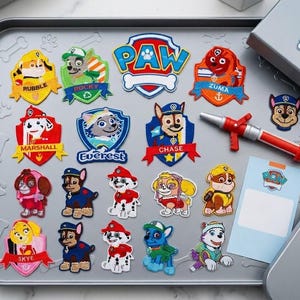 Könnte beinhalten: Eine Sammlung von Paw Patrol Stickaufnähern mit Charakteren wie Rubble, Rocky, Zuma, Marshall, Everest, Chase und Skye, zusammen mit einem roten und silbernen Feuerlöscher-Spielzeug aus Kunststoff und einer rechteckigen Karte auf einem grauen Metalltablett.