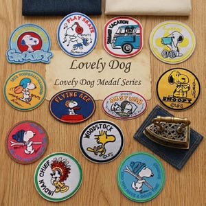 May include: A collection of twelve circular and oval embroidered fabric patches featuring Snoopy and Woodstock characters in various activities, arranged around a central paper sign with the text Lovely Dog Lovely Dog Medal Series.