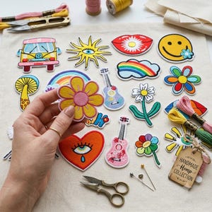 Könnte beinhalten: Eine Sammlung bunter gestickter Aufnäher mit verschiedenen Motiven, darunter ein gelber Van, eine Sonne mit Auge, rote Lippen, ein Smiley, ein Regenbogen, ein Pilz, Gitarren, Blumen und ein Herz mit Auge, zusammen mit Stickgarn und einer Schere.
