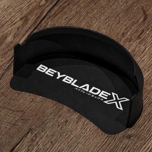 Könnte beinhalten: Ein schwarzes, halbkreisförmiges Kunststoff-Wandelement für ein Beyblade X Stadion mit dem weißen Beyblade X Logo und japanischem Text auf der Innenseite. Die geschwungene Struktur hat eine glatte Oberfläche und eine erhöhte Kante an der Oberseite.