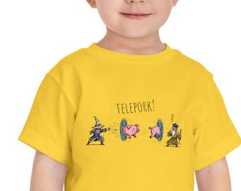 May include: A bright yellow short-sleeve t-shirt featuring a graphic print of two wizards casting spells on a pig that is teleporting between two portals. The text "TELEPORK!" is printed above the graphic in a simple, dark, handwritten-style font.