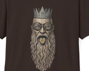 May include: A dark brown short-sleeve t-shirt featuring a centered graphic of a bearded person wearing a crown and round glasses. The person has their mouth open with a small gold-colored square object resting on their tongue, centered on the chest.