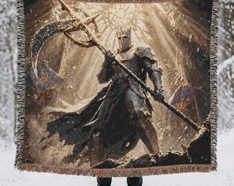 May include: A woven throw blanket featuring a detailed depiction of a knight in full armor holding a large scythe. The knight wears a crown and stands in a dark, atmospheric setting with golden light rays. The blanket has a fringed edge.