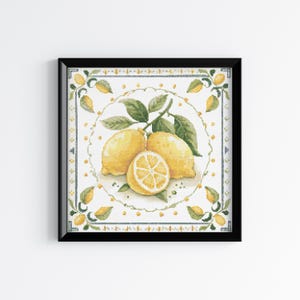 May include: A square cross-stitch embroidery in a black frame featuring a central circular design of two whole yellow lemons and one halved lemon with green leaves. The border is decorated with small yellow lemon motifs and blue lines.