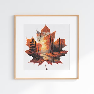 Könnte beinhalten: Ein gerahmtes Kreuzstichmuster in Form eines Ahornblatts, das eine detaillierte herbstliche Waldlandschaft mit orangefarbenen, roten und braunen Bäumen, einem ruhigen Bach und einem Sonnenuntergangshimmel zeigt, in einem hellen Holzrahmen.