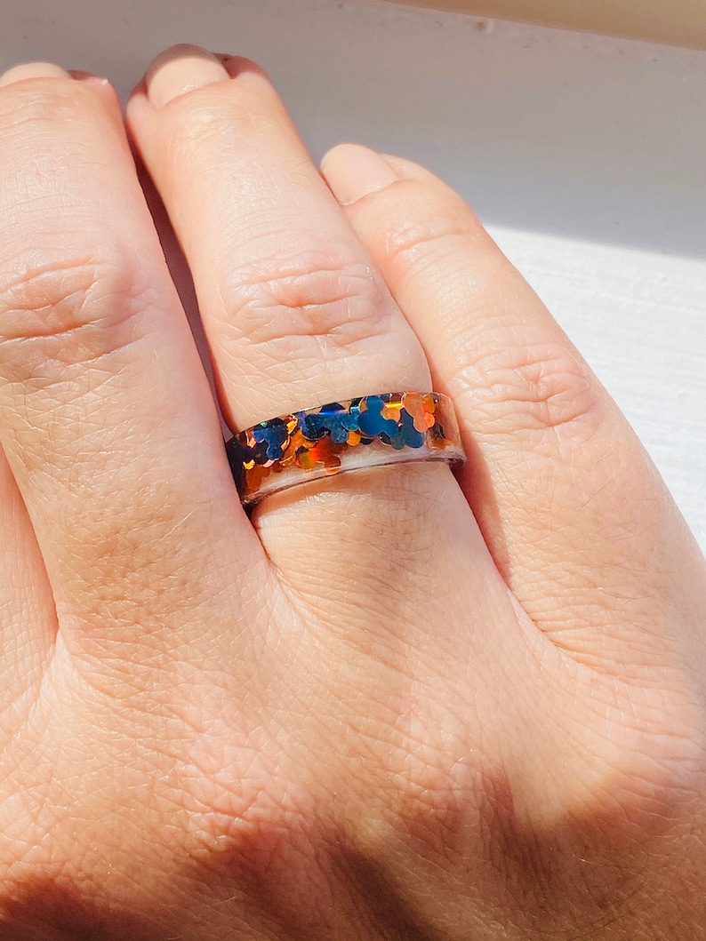 Puede incluir: Un anillo con una banda transparente y una capa de purpurina iridiscente en tonos azules, naranjas y dorados.