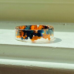Puede incluir: Un anillo de resina transparente con purpurina negra y naranja incrustada en su interior.