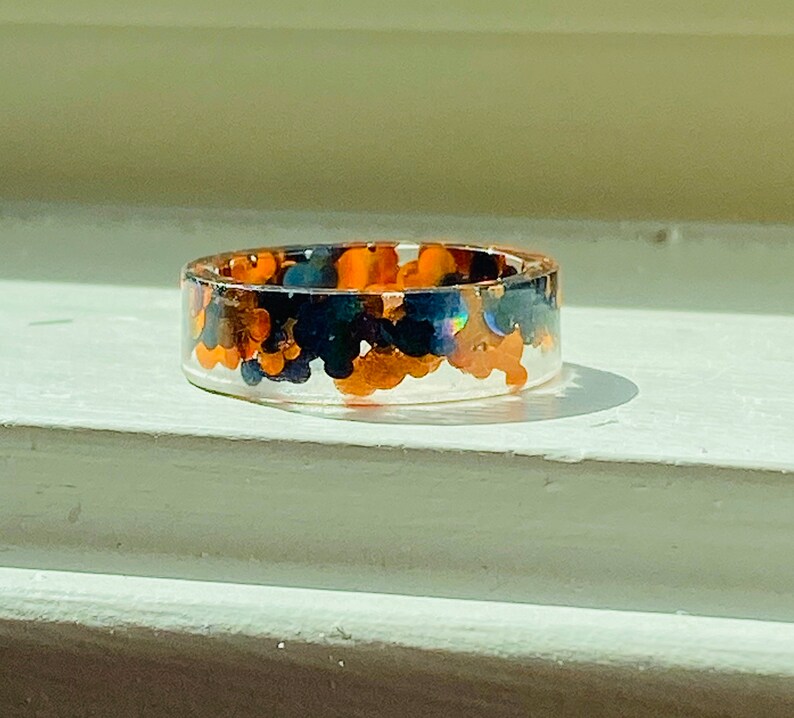 Puede incluir: Un anillo de resina transparente con purpurina negra y naranja incrustada en su interior.