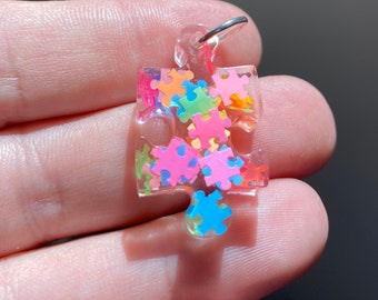 May include: A clear resin puzzle piece charm with a silver loop. The charm is filled with colorful puzzle pieces in shades of pink, blue, green, and orange.