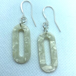 May include: A pair of oval-shaped earrings with a white marbled finish and silver hooks.