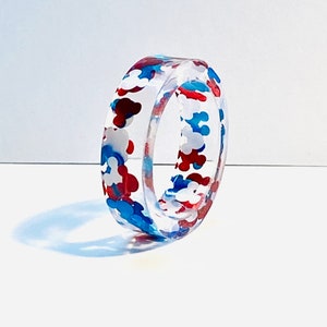 May include: A clear resin ring with a red, white, and blue confetti pattern.