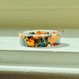 Puede incluir: Un anillo de resina transparente con un dise&ntilde;o colorido con cabezas de Mickey Mouse. El anillo est&aacute; lleno de cabezas de Mickey Mouse de color naranja, amarillo, azul, verde y negro.