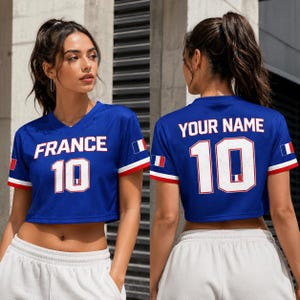 以下が含まれることがあります： 白文字で「FRANCE」と数字の「10」がプリントされた青色のクロップトップジャージ。袖には赤と白のトリムと小さなフランス国旗が付いています。ジャージの背面には「YOUR NAME」と数字の「10」がプリントされています。