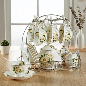 Peut inclure: Un service à thé en porcelaine blanche orné d'un motif floral de fleurs jaunes et blanches avec un liseré doré. L'ensemble comprend une théière, un pot à lait, un sucrier, des tasses et des soucoupes, disposés sur un support en fil chromé.