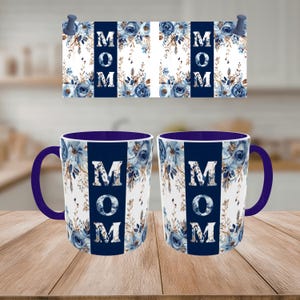 Könnte beinhalten: Zwei Keramikbecher mit floralem Design und dem Wort "MOM" in weißen Buchstaben auf marineblauem Hintergrund. Die Becher haben einen marineblauen Innenraum und Henkel. Eine passende Dekotafel mit dem gleichen Design ist über den Bechern befestigt.