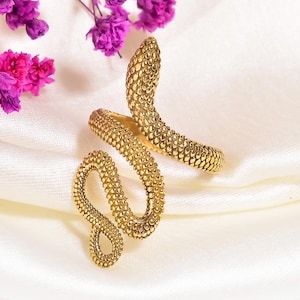 May include: A gold-toned ring shaped like a coiled snake with a textured, scale-like surface. The design features a winding body that wraps around, with the head of the snake positioned at the top and the tail forming a loop at the bottom.