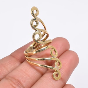 May include: A gold-toned metal ring featuring an elongated, openwork design that extends vertically along the finger. The piece is constructed from smooth, polished metal bands that curve into swirling, scroll-like patterns throughout.