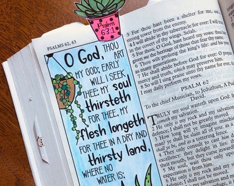May include: A page from a Bible with a hand-drawn illustration of three potted succulents. The text on the page reads "O God, thou art my God; early will I seek thee: my soul thirsteth for thee, my flesh longeth for thee in a dry and thirsty land, where no water is."  The illustration is in a watercolor style with pink, yellow, and green colors.